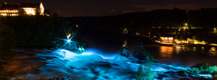 Illuminated city by river against sky at night