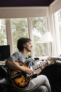 Side view of man practicing guitar while sitting at home