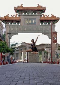 Woman jumping on footpath against historic structure