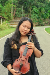 Portrait of young woman holding violin at park