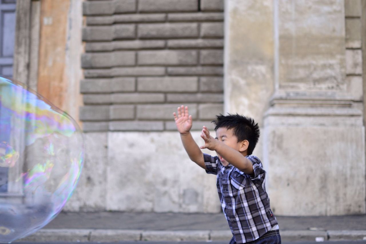 SIDE VIEW OF A BOY PLAYING WITH BUBBLES IN PARK