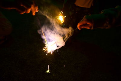 Cropped hands of people burning sparklers at night