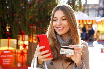 Woman paying her presents with smartphone with christmas markets with boxes on the background