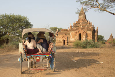 People traveling from cart on dirt road against temple