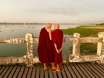 Rear view of monks standing by railing against sea and sky