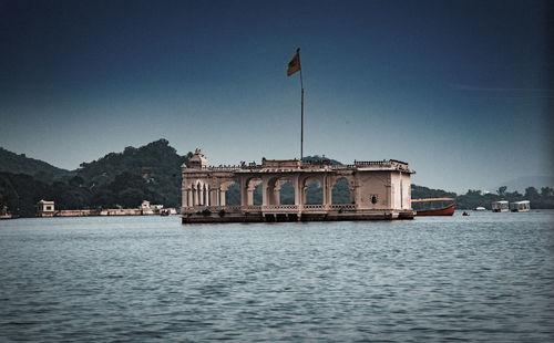 Buildings by river against clear blue sky