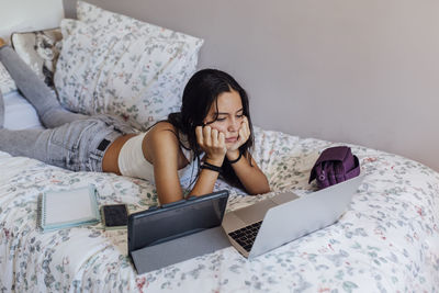 Girl with head in hands watching laptop on bed at home