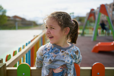 Little girl smiling as she leans on the playground fence
