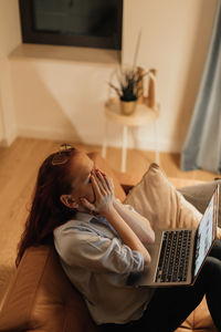 Young woman using laptop while sitting on bed at home