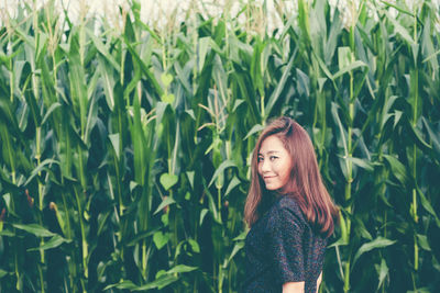 Portrait of smiling woman standing against crops in farm