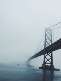 Bay bridge over sea against sky during foggy weather