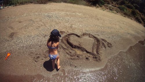 Rear view of girl standing by heart shape on sand at beach