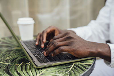 Hands of freelancer typing on laptop sitting at sidewalk cafe