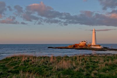 Lighthouse on island in sea against sky during sunset