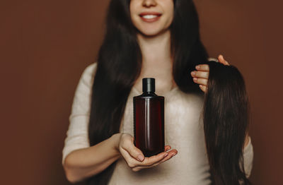 Midsection of woman holding shampoo against colored background