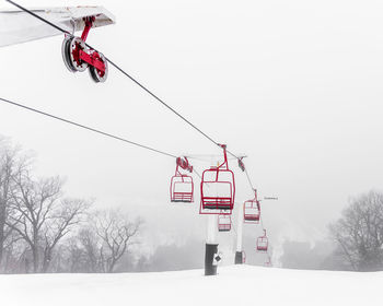 Low angle view of ski lift over snow covered trees against sky