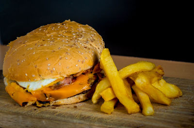 Close-up of burger with french fries on serving board against black background