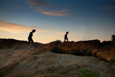 Side view of two people walking on rocky landscape