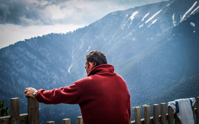 Rear view of man standing on snowcapped mountain against sky