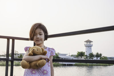 Portrait of girl holding teddy bear against sky