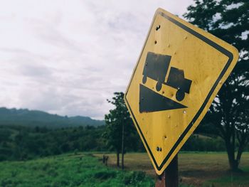 Information sign on road amidst field against sky