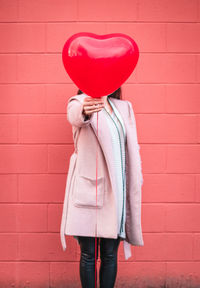 Woman holding heart shape balloon against wall