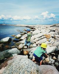 People sitting on rock by sea against sky