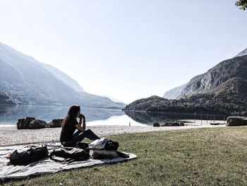 People sitting on rock by lake against sky