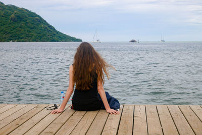 Rear view of woman sitting on pier over sea against sky