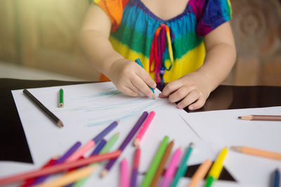 Midsection of woman with multi colored pencils on table