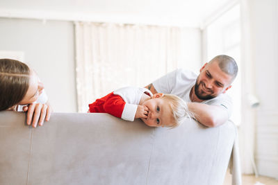 Young happy family on bed in bright living room. man and woman in love with cute little baby girl 