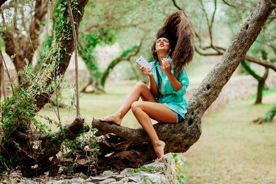 Young woman using phone while sitting on tree trunk