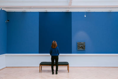 Rear view of woman standing against blue wall