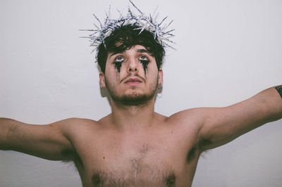 Close-up of shirtless man with make-up standing against wall