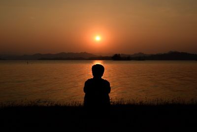 Silhouette man standing by lake against sky during sunset