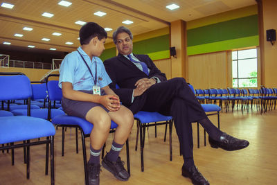 Professor talking with boy while sitting on chairs