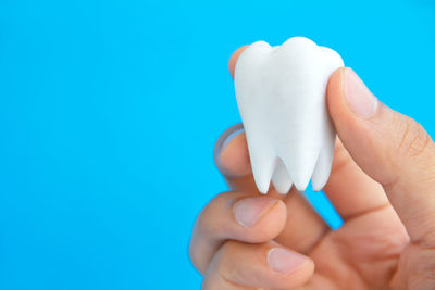 Cropped hand holding dentures against blue background