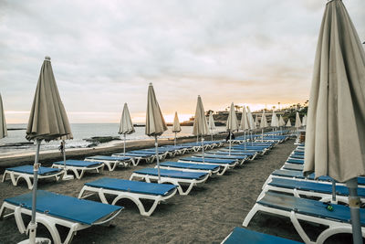 Empty seats at beach against cloudy sky