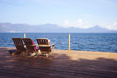 Chairs on deck chair by sea against sky