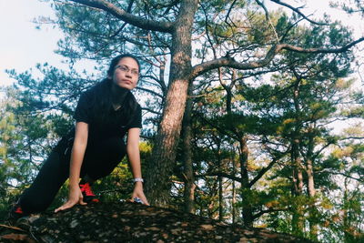 Low angle view of young woman exercising against trees in forest