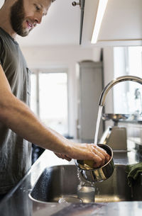 Man washing sauce pan with scouring pad at sink