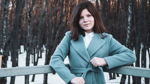 Portrait of beautiful young woman standing by railing in winter