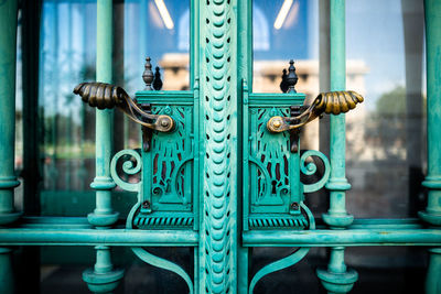 An old iron door handle at a huge double door and glasses between some small iron columns.