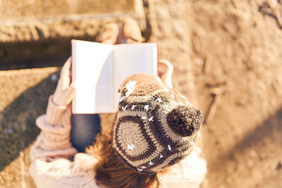 Beautiful woman with cap reading a book in a park at winter or spring sunset.