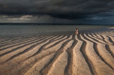Shirtless girl sitting at beach against cloudy sky during sunset