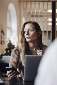 Businesswoman looking away while talking through smart phone at office