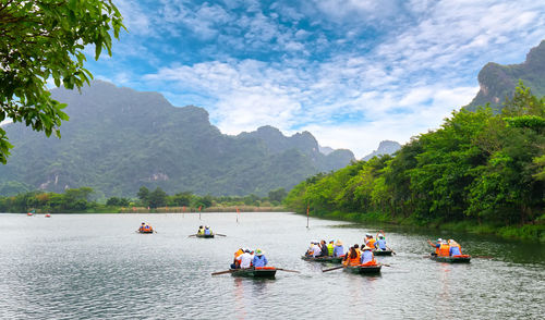 People on boats in river against mountains