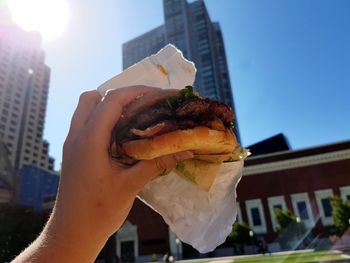 Person holding hamburger against skyscrapers 