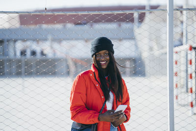 Portrait of smiling young woman standing by fence