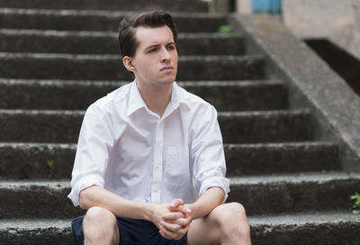 Young man looking away while sitting on staircase